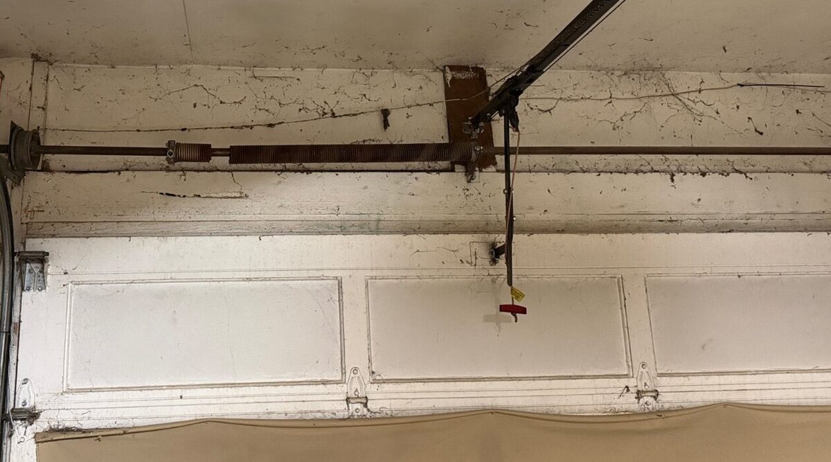 Old rusted torsion spring above a garage door before replacement