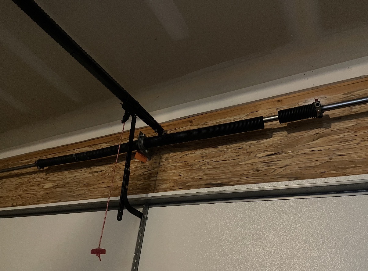 Broken garage door torsion spring on the header above the door, with a visible gap in the spring coils